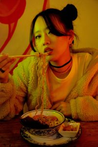 Young woman in hooded jacket eating noodles at a cafe